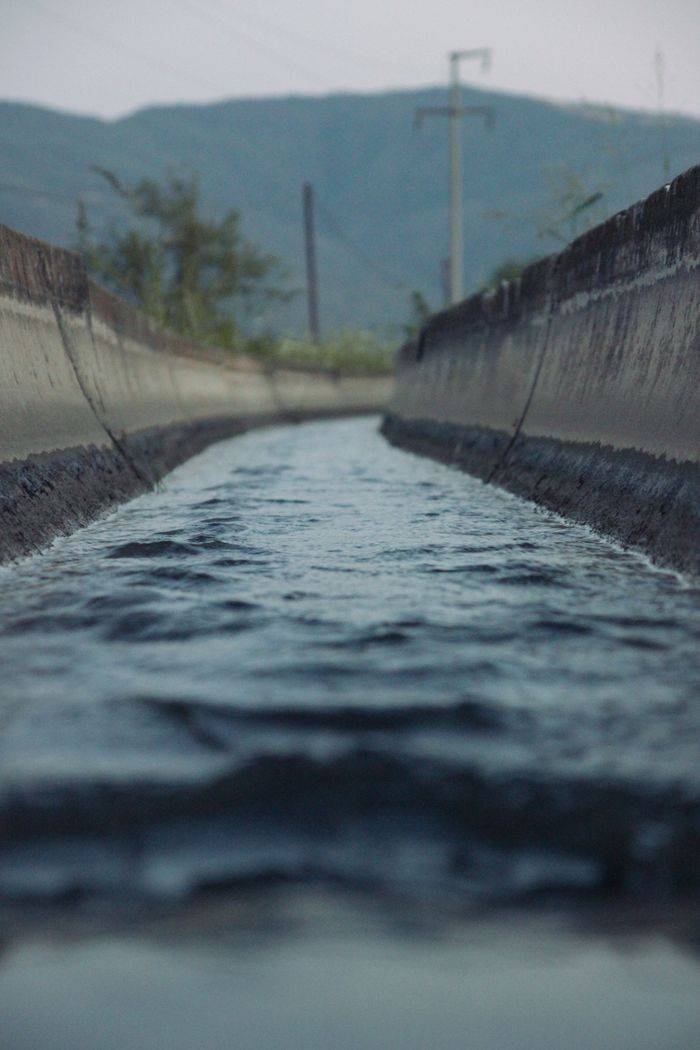 Close-up shot of water flowing through a concrete channel with mountains in the background.